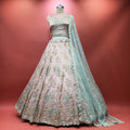 Baby pink lehenga on mannequin with multicolor floral embroidery and sheer teal dupatta