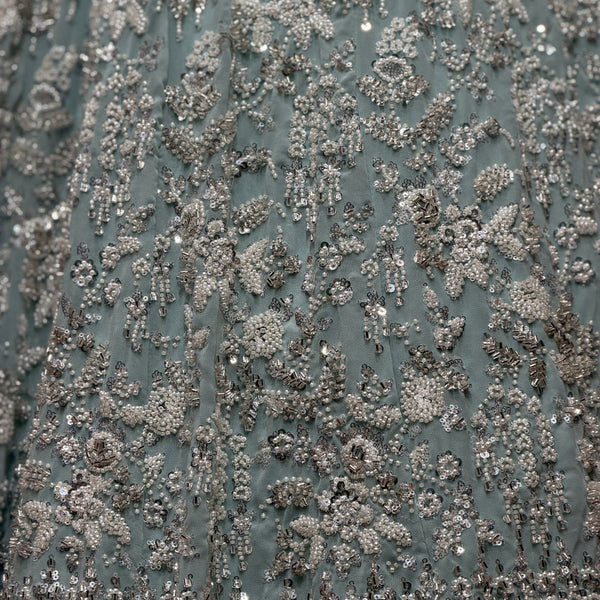 Close-up of sky blue fabric covered in silver beadwork floral vine pattern