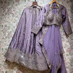 Lavender raw silk lehenga, embroidered blouse and dupatta on hangers against floral wallpaper