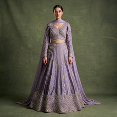 Model in a lavender raw silk lehenga with slim embroidered floral lines, a scalloped arch hem, full-sleeve V-neck blouse with beaded drops and a matching dupatta against an olive backdrop