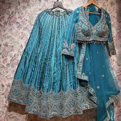 Teal raw silk lehenga with embroidered floral lines and scalloped hem, embroidered blouse and net dupatta on hangers