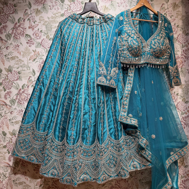 Teal raw silk lehenga with embroidered floral lines and scalloped hem, embroidered blouse and net dupatta on hangers