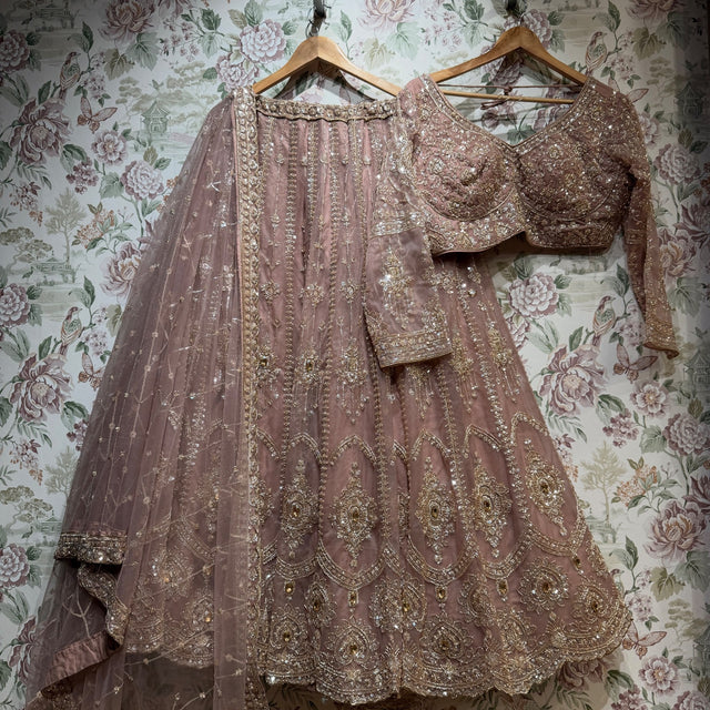 Mauve lilac net lehenga, embroidered full-sleeve blouse and net dupatta on hangers against floral wallpaper