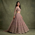 Model in a mauve lilac net lehenga with vertical bead lines, stone-set medallions and a scalloped hem, a full-sleeve V-neck blouse and a net dupatta against an olive backdrop