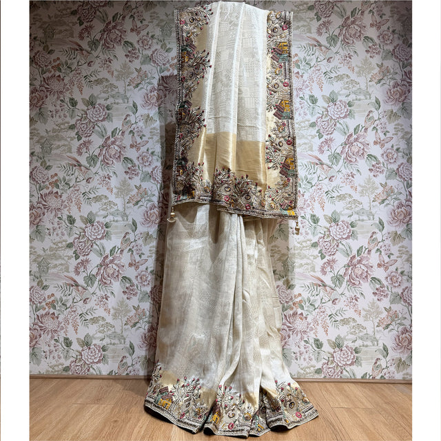 Off white viscose silk saree displayed full length with woven tone-on-tone pattern, gold tissue bands, embroidered house and tree border and gold tassels