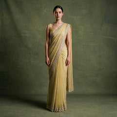 Model in a lemon yellow chiffon saree with a cutdana and bead patterned border along the pallu and hem, against an olive backdrop