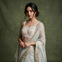 Close-up of the mint viscose linen saree draped over the shoulder, showing the gold check, zari border and the ivory sleeveless blouse with pink and peach floral handwork