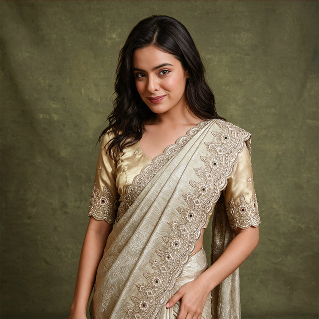 Champagne tissue saree with scalloped leaf and flower handwork border draped over the shoulder, worn