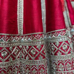 Close-up of red lehenga fabric with silver-gold geometric embroidery and beadwork trim.