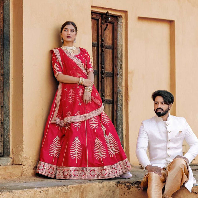 Red lehenga with gold-trimmed neckline, three-quarter sleeves, and heavily embroidered skirt