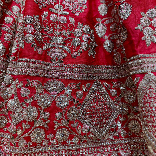 Close-up of red lehenga fabric with silver-toned floral embroidery and detailed border