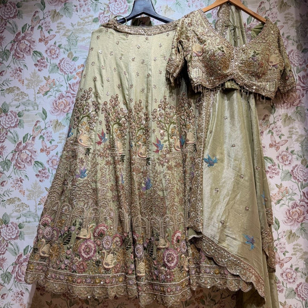 Pista green lehenga set laid flat: skirt with swan hem band, heavy blouse and bluebird-motif dupatta