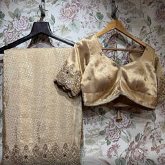 Folded champagne gold saree with beaded scalloped hem border beside the stitched gold blouse with floral motifs and embroidered sleeve cuffs, on hangers