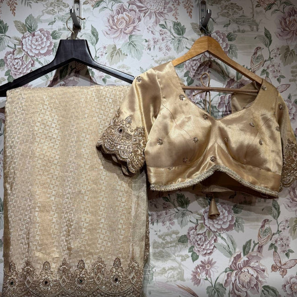 Folded champagne gold saree with beaded scalloped hem border beside the stitched gold blouse with floral motifs and embroidered sleeve cuffs, on hangers