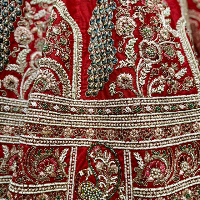 Detail of the red lehenga with a teal beaded peacock, floral vines and stacked pearl and zari hem bands