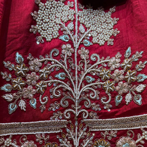 Close-up of cherry red lehenga: white pearl clusters, gold zari coils and pink, mint and mustard resham flowers