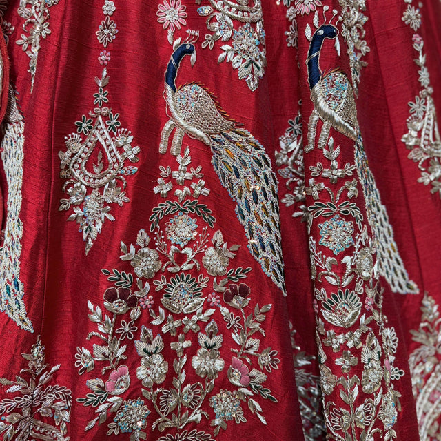 Red silk lehenga fabric with detailed silver and multicolor peacock and floral embroidery