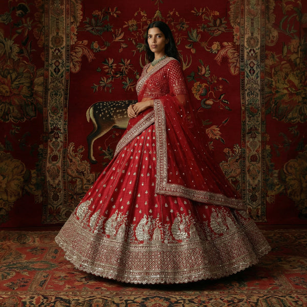 Red bridal lehenga with silver-toned peacock motif border and ornate hem