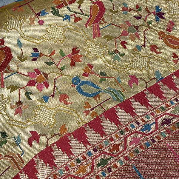 Gold saree fabric close-up with colorful parrot-and-floral jaal pattern, pink border