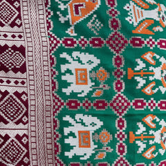Green and maroon patola motif silk fabric with geometric pattern and zari border detail.