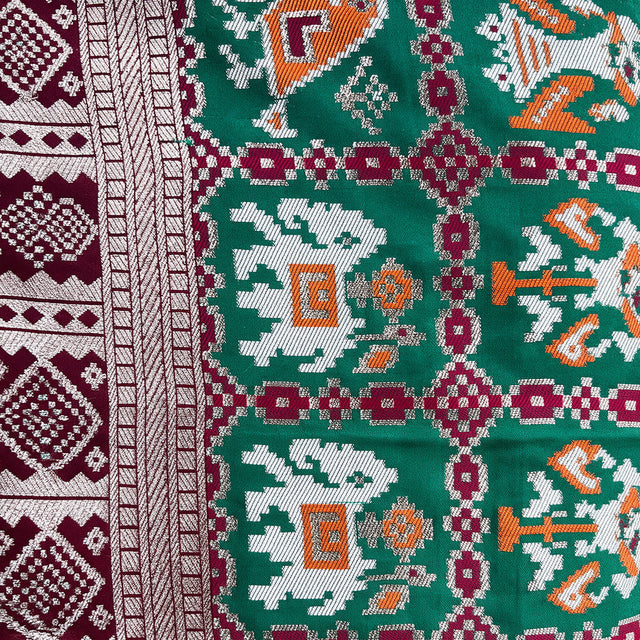 Green and maroon patola motif silk fabric with geometric pattern and zari border detail.
