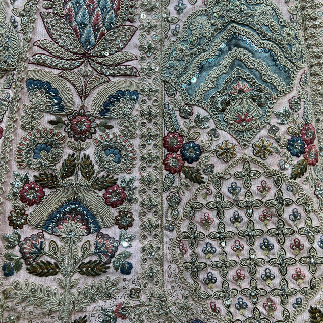 Close-up of ornate floral and paisley embroidery on pale fabric with teal, pink, and red details