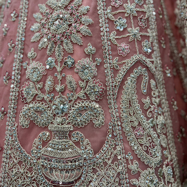 Close-up of dusty pink fabric with teal-and-gold floral embroidery and beadwork