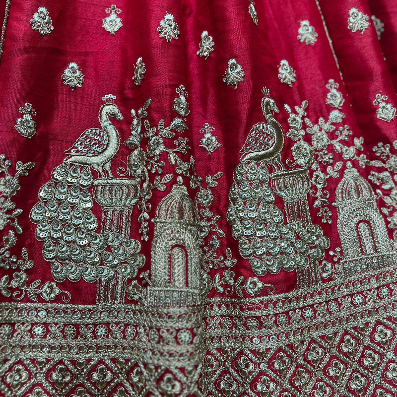 Red lehenga fabric close-up with silver peacock and temple motifs, embroidered border