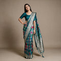 Teal-blue silk saree with patchwork panels and zari floral border, draped look